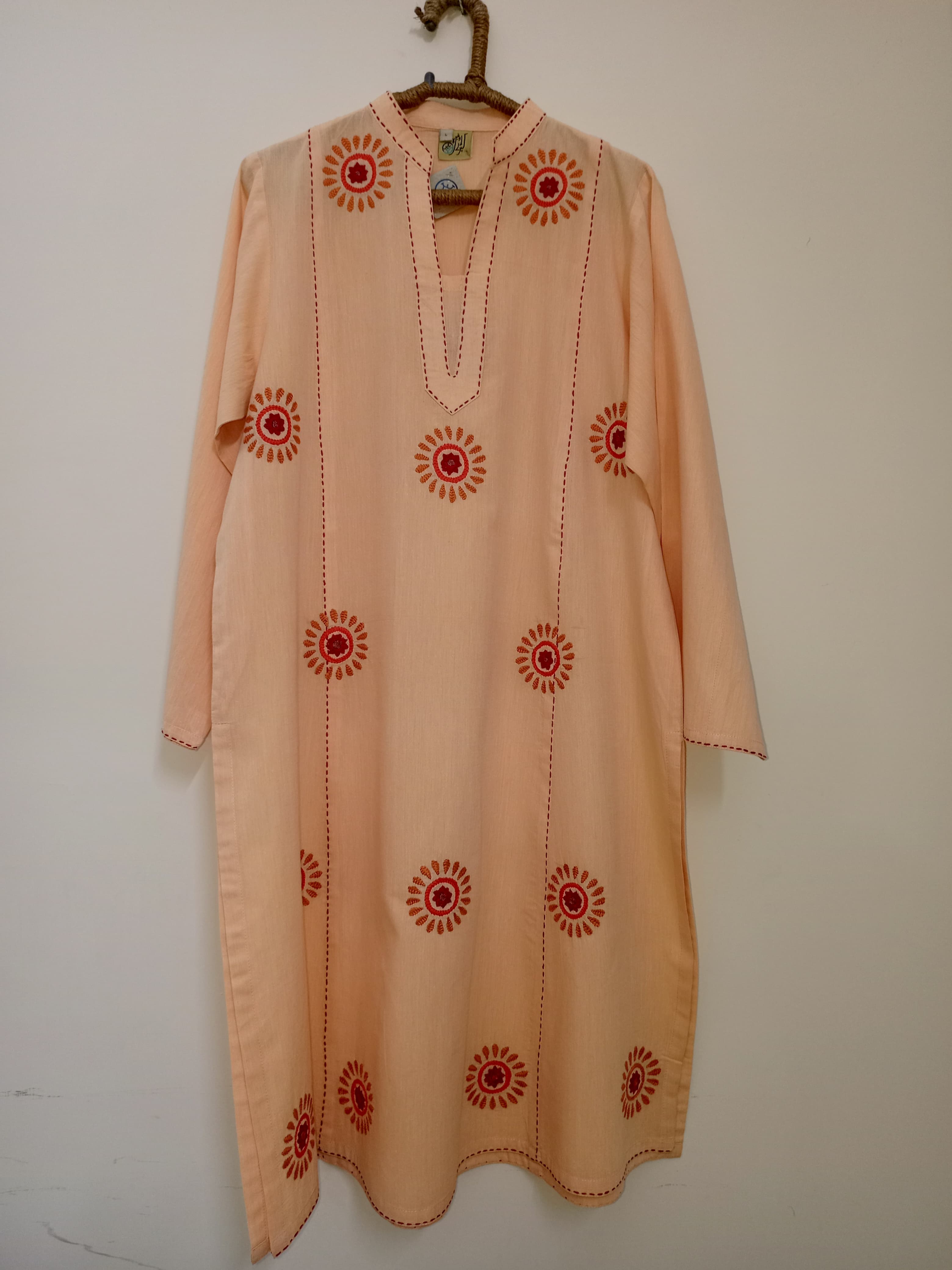 Peach shirt with scattered floral embroidery, soft fabric, and a light pastel base that highlights minimalism with gentle handcrafted detail.